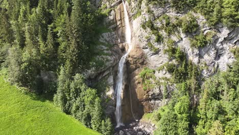 Drone-view-of-Klöntalersee-valley-and-lake-in-Glarus-Süd,-Switzerland,-featuring-a-summer-waterfall-and-sunlit-rocks