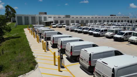 Slowly-dropping-low-drone-shot-of-a-row-of-USPS-delivery-trucks-behind-large-post-office-next-to-row-of-newly-installed-electric-vehicle-chargers-in-preparation-of-NGDV-electric-trucks