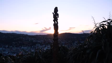 Estatua-Cultural-Maorí-Tallada-De-Pou-Whenua-Con-Vista-A-La-Ciudad-Capital-De-Wellington-Durante-La-Brillante-Puesta-De-Sol-En-Aotearoa,-Nueva-Zelanda