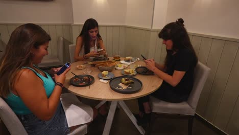 Tres-Mujeres-En-Un-Café-Usando-Teléfonos-Inteligentes-Durante-Una-Comida