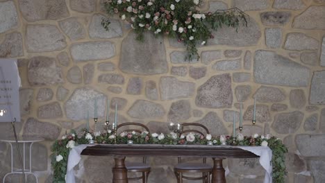 Mesa-De-Novios-Para-Una-Boda-Romántica-Con-Arreglos-Florales,-Colocada-Frente-A-Una-Pared-De-Piedra-Rústica