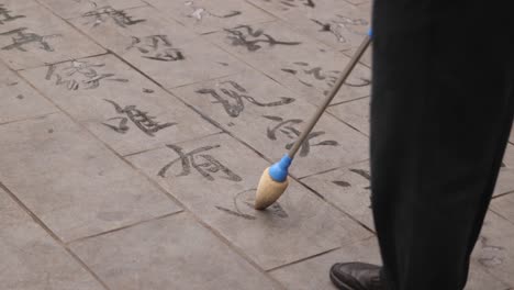 A-man-painting-Chinese-letters-on-a-street-with-a-brush-in-Chengdu,-China