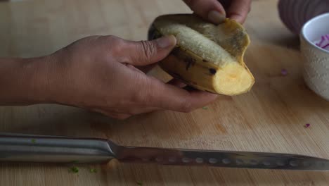 Slicing-off-the-skin-of-a-yellow-plantain-and-special-ingredients-to-cook-a-meal-two-cans-of-beans-rice-plantain-avocado-red-onion-and-cilantro