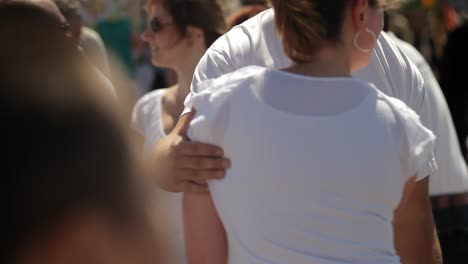 A-tall-man-with-sunglasses-and-a-woman-in-a-white-t-shirt-dance-salsa-during-a-summer-festival,-sharing-a-joyful-moment-amidst-the-lively-crowd