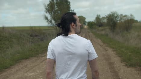 Man-walking-on-dirt-road-by-expansive-fields