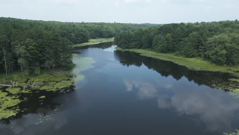 Drone-pulls-back-over-calm-peaceful-lake-reflecting-clouds-in-sky-as-trees-surround-water,-Lake-Fitzgerald-Northampton-Massachusetts