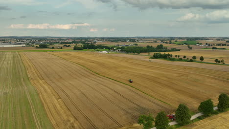 Vista-Aérea-De-Un-Vasto-Campo-De-Trigo-Después-De-La-Cosecha,-Con-Un-Solo-Tractor-En-La-Distancia.