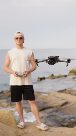 Vertical-shot-of-male-drone-pilot-fly-aircraft-near-beach,-Mallorca