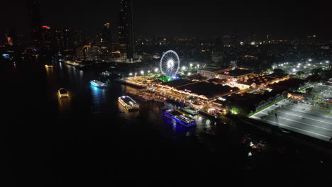 Drohne-Umkreist-Das-Beleuchtete-Asiatische-Flussufer,-Nacht-In-Bangkok,-Thailand