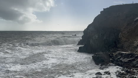 Clouds-part-and-remnants-of-storm-waves-crash-into-sea-cliff-rocks