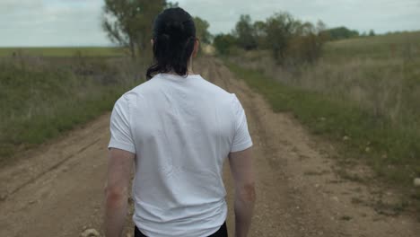 Man-walking-on-dirt-road-by-expansive-fields