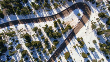 An-overhead-shot-of-a-winding-mountain-road-cutting-through-a-snow-covered-forest,-with-a-lone-car-navigating-the-turns