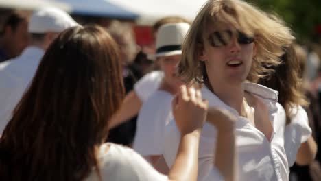 A-white-couple-in-white-t-shirts-dance-salsa-at-a-summer-festival,-turning-each-other-joyfully-amidst-a-lively-crowd