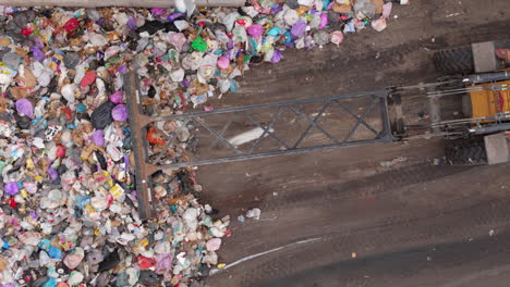 Gulls-fly-above-dozer-pushing-plastic-trash-bags-onto-heap-at-landfill,-aerial