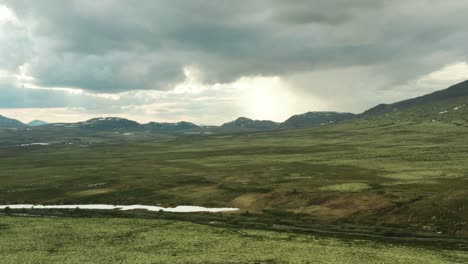 Panoramic-aerial-establishing-rises-above-grassland-plains-of-Rondane-National-Park-Innlandet-county-Norway-as-sunlight-breaks-between-clouds