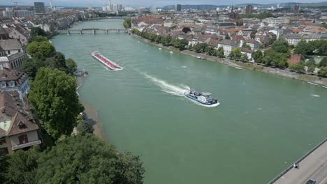 4K-Drone-Video-of-Tugboat-Pulling-Cargo-Barge-Towards-the-Wettsteinbrücke-Bridge-over-the-Rhine-River-in-Basel,-Switzerland