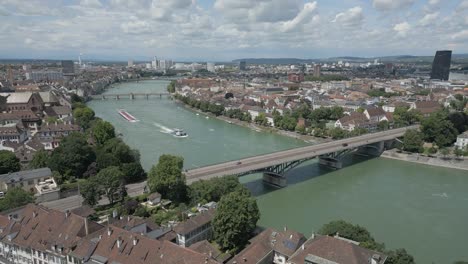 4K-Drone-Video-of-Tugboat-Pulling-Barge-Towards-the-Wettsteinbrücke-Bridge-over-the-Rhine-River-in-Basel,-Switzerland