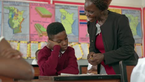 Maestra-Ayudando-A-Un-Estudiante-En-Clase-En-Una-Escuela-En-Uganda---Primer-Plano