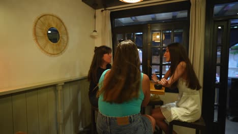 Three-women-having-an-informal-conversation-at-a-cozy-cafe-after-work,-evening-indoor-setting