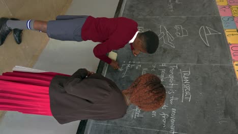 African-Boy-Writes-On-The-Blackboard-At-School---Vertical-Shot