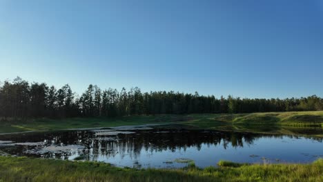 Golden-light-casts-a-serene-glow-over-tranquil-waters,-reflecting-lush-greenery-and-the-peaceful-ambiance-of-Yakutia’s-pristine-wilderness-at-dusk