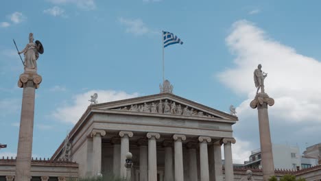 Seitliche-Ansicht-Der-Akademie-Von-Athen-Mit-Der-Griechischen-Flagge,-Die-Stolz-Im-Wind-Weht