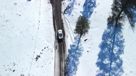 Eine-Drohne-Von-Oben-Nach-Unten-Verfolgt-Einen-LKW,-Der-Auf-Einer-Schlammigen,-Mit-Schnee-Bedeckten-Schotterstraße-Durch-Schlammpfützen-Zur-Autobahn-Fährt