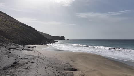 Toma-Aérea-De-Las-Olas-Del-Océano-Rompiendo-En-La-Playa-Vacía-De-Una-Isla-Volcánica-Desierta-A-60-Fps