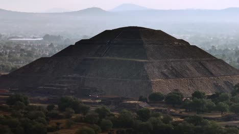 Close-up-drone-aerial-view-of-the-Pyramid-of-the-Sun-at-dawn,-surrounded-by-mist-and-lush-green-trees