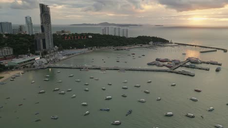 Skyscraper-landmark,-sailboats-at-Pattaya-Thailand-famous-beach-Sunset-drone-sky-shot