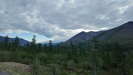 Discover-the-serene-beauty-of-Yakutia,-where-towering-mountains-and-vibrant-greenery-come-together-under-a-dramatic-sky