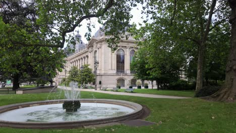 Petit-Palais-art-museum-side-building-through-tree-leaves-with-the-surrounding-park-and-fountain-in-Paris,-France