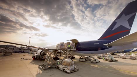 Sunset-at-airport-with-cargo-being-loaded-onto-aircraft,-vibrant-sky-and-busy-tarmac-scene,-wide-shot