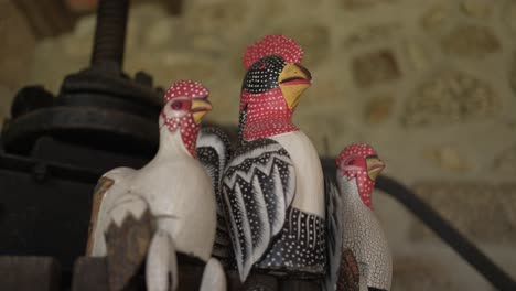 Colorful,-handcrafted-rooster-figurines-with-intricate-patterns,-displayed-against-a-rustic-stone-wall