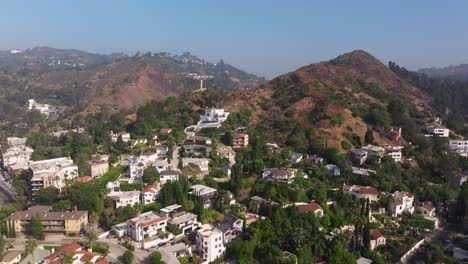 Panoramic-aerial-dolly-over-dense-trees-covering-sidewalks-up-mountain-side-of-hills-in-Los-Angeles-California-with-cross-looking-down