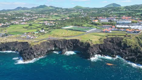 Coastal-cliffs-with-vibrant-blue-water-and-lush-green-landscape,-aerial-view