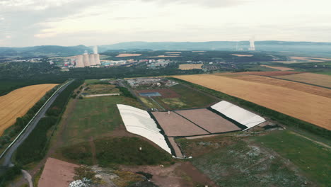 High-quality-footage-of-landfill-with-flyover-geomembrane,-drone-cruising,-nature-surrounding-energy-plant-chimneys,-showcasing-environmental-themes