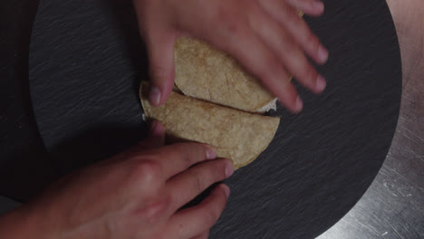 Beautiful-slow-motion-shot-from-a-high-angle-of-a-chef-folding-Mexican-tortillas-with-shredded-chicken-with-his-hands-to-present-the-dish-of-enchiladas-in-green-sauce