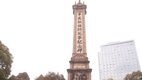 Obelisk-in-Chengdu,-China-standing-tall-with-traditional-inscriptions-and-surrounded-by-trees-and-modern-buildings