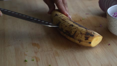 Yellow-plantain-skin-being-cut-and-peeled-and-special-ingredients-to-cook-a-meal-two-cans-of-beans-rice-plantain-avocado-red-onion-and-cilantro