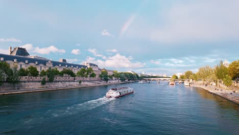 Herrlicher-Blick-Auf-Die-Ausflugsboote,-Die-Sich-Entlang-Der-Seine-Bewegen,-Beleuchtet-Vom-Sonnenuntergang-Mit-Der-Regenbogenbedeckten-Skyline-Von-Paris-Im-Hintergrund