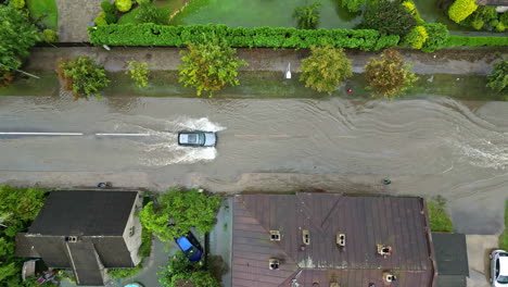 Top-down-drone-shot-of-a-car-driving-through-flooding-water-on-suburban-streets