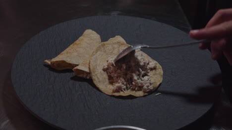 Beautiful-slow-motion-and-close-up-shot-as-shredded-chicken-is-served-inside-a-Mexican-tortilla-on-a-black-plate-as-a-presentation-for-the-Mexican-dish-enchiladas-in-green-sauce-prepared-by-a-chef