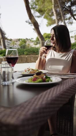 Toma-Vertical-De-Una-Atractiva-Mujer-Bebiendo-Vino-Durante-El-Almuerzo-En-Un-Café-Al-Aire-Libre