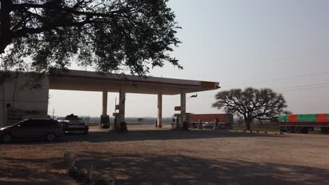 A-Vintage-shell-style-gas-station-establishing-of-a-wild-dry-landscape-of-Argentine-meadows-at-Entre-rios-province,-during-windy-daylight,-trees-branches-in-motion