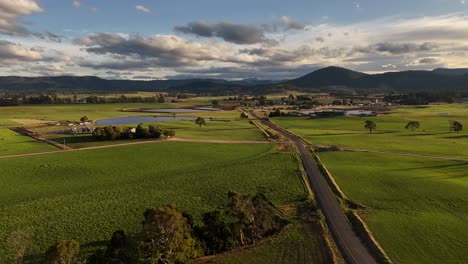 Rural-road-crossing-green-fields,-Tasmania-at-sunset,-Australia