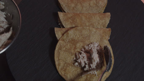 Beautiful-slow-motion-close-up-shot-of-a-chef's-hands-serving-shredded-chicken-from-a-bowl-onto-tortillas-inside-an-industrial-kitchen-at-a-Mexican-restaurant