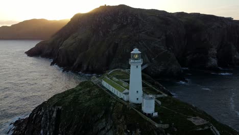 Birds-passing-South-Stack-lighthouse-aerial-view-circling-island-landmark-sunrise-mountains