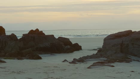 Pequeñas-Rocas-En-La-Playa-Con-El-Océano-De-Fondo-Al-Atardecer