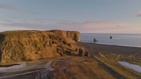 Playa-De-Dyrhólaey-Y-Formación-Rocosa-Con-El-Faro-De-Dyrhólaeyjarviti,-Vista-Aérea